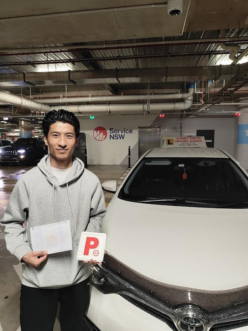 New driver holding his P plate beside the driving school car after passing his test