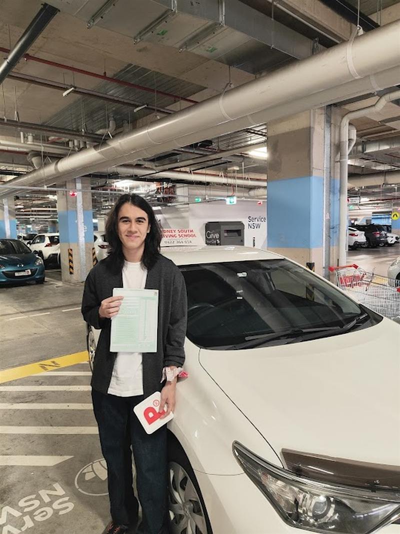 Learner driver with his passed test result beside the automatic driving school car