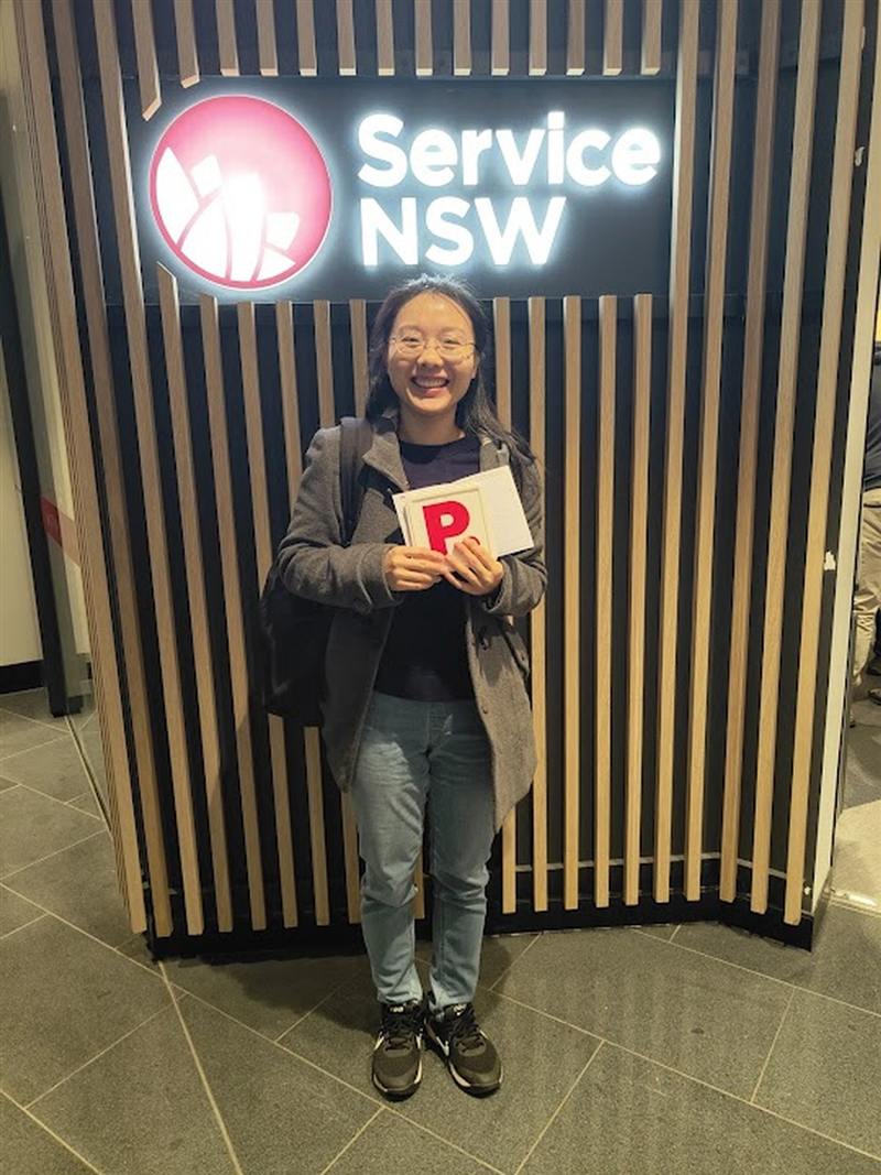 Smiling learner driver holding her new P plates at Service NSW after driving lessons in Liverpool